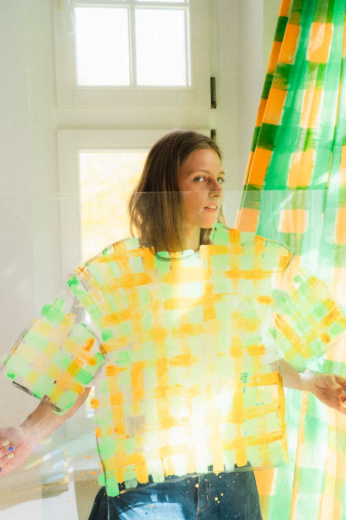 Rika in the studio, holding up a hand-painted tangerine and green gingham T-shirt
